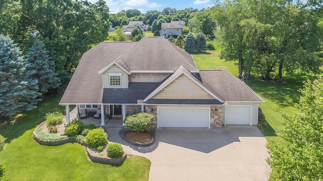 view of front facade with stone siding, covered porch, concrete driveway, a front yard, and an attached garage