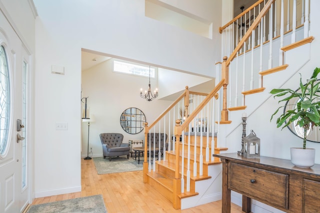 foyer with baseboards, stairs, hardwood / wood-style flooring, an inviting chandelier, and a towering ceiling