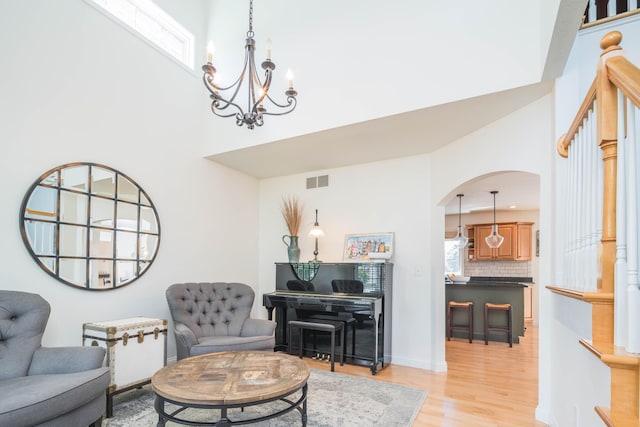 living area with light wood-type flooring, visible vents, arched walkways, baseboards, and a towering ceiling