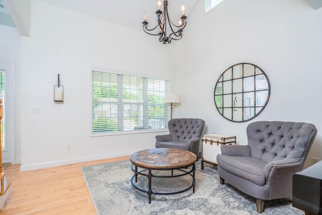 living area featuring an inviting chandelier, a high ceiling, light wood-type flooring, and baseboards