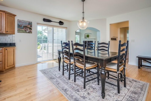 dining space with arched walkways, a fireplace, light wood-style floors, and baseboards