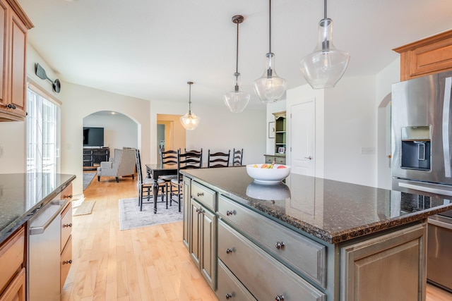 kitchen with a center island, dark stone counters, arched walkways, light wood-style floors, and appliances with stainless steel finishes