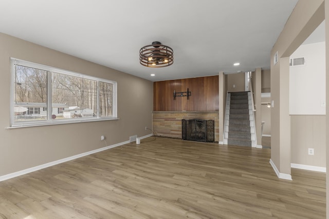 unfurnished living room featuring light wood-type flooring, visible vents, a fireplace, and stairs