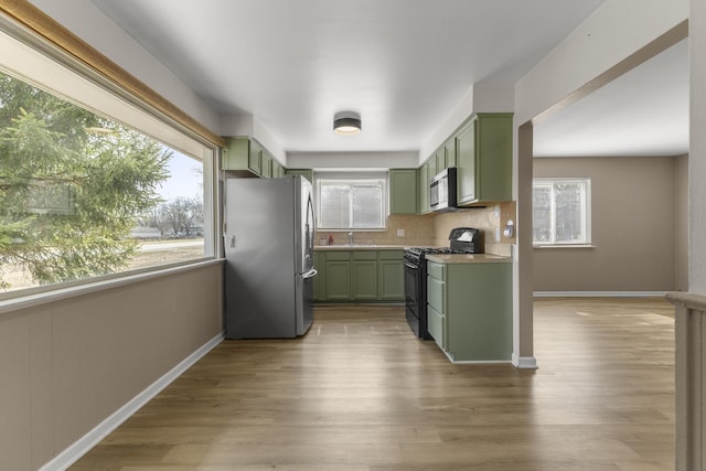 kitchen with stainless steel appliances, wood finished floors, green cabinets, and decorative backsplash