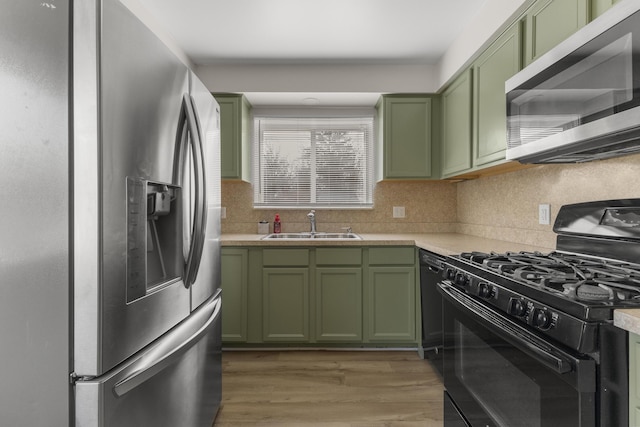 kitchen featuring green cabinets, light countertops, light wood-style floors, stainless steel appliances, and a sink