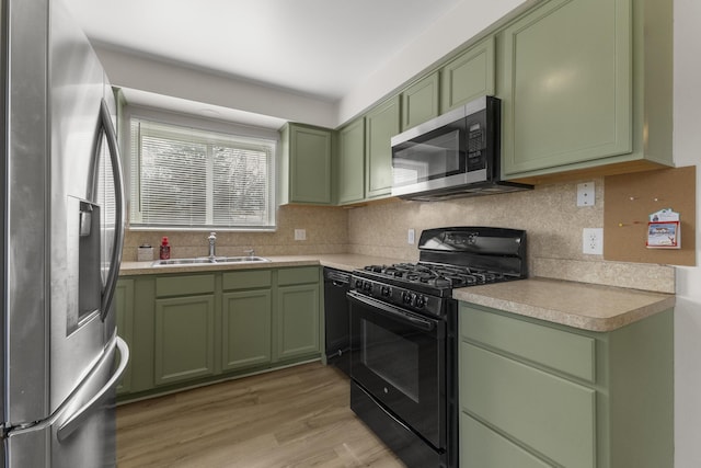 kitchen with black appliances, light wood-style flooring, a sink, backsplash, and green cabinets