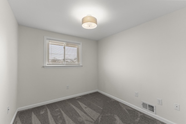 spare room with dark colored carpet, visible vents, and baseboards