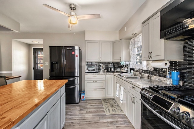 kitchen featuring tasteful backsplash, butcher block countertops, black refrigerator with ice dispenser, stainless steel gas range, and a sink