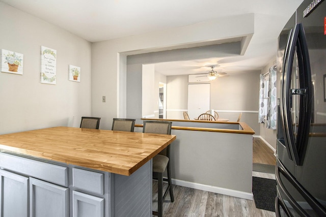 kitchen featuring wood finished floors, a breakfast bar, ceiling fan, black fridge with ice dispenser, and wood counters