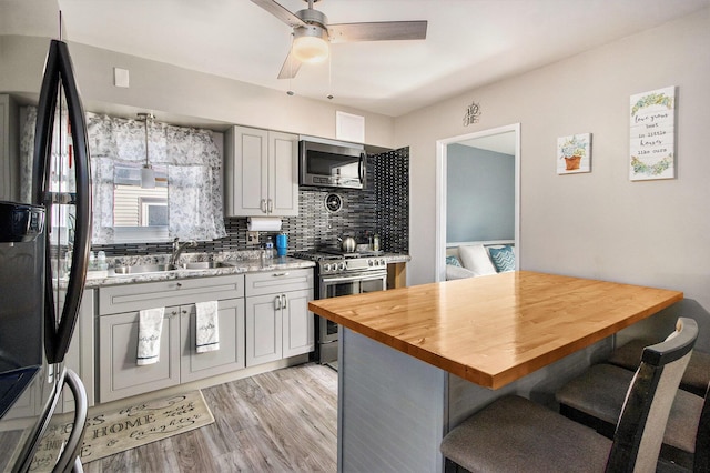 kitchen featuring light wood-type flooring, a sink, a kitchen breakfast bar, stainless steel appliances, and wooden counters