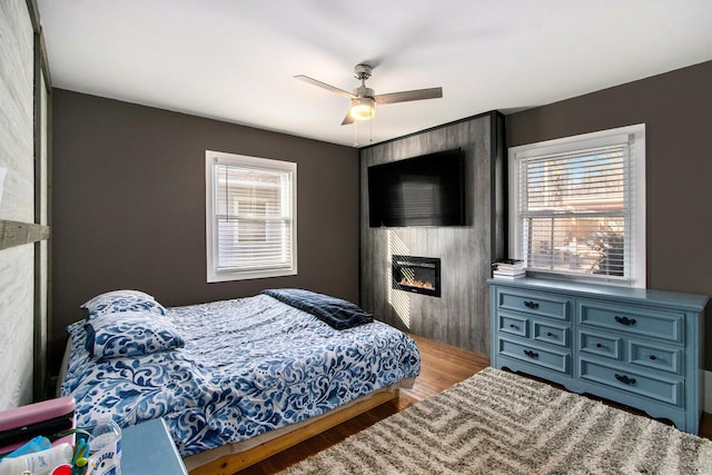 bedroom with ceiling fan, a large fireplace, and wood finished floors