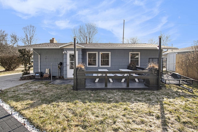 rear view of property with a chimney, a lawn, a wooden deck, and a shingled roof