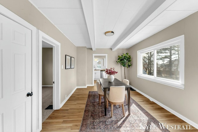 dining space with beam ceiling, light wood-style floors, and baseboards