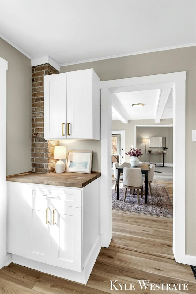 kitchen with butcher block countertops, light wood-style flooring, ornamental molding, white cabinetry, and baseboards