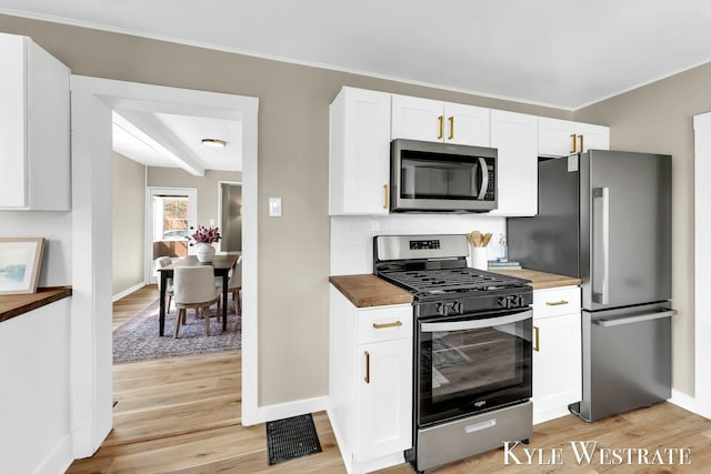 kitchen with baseboards, stainless steel appliances, wood counters, white cabinetry, and light wood-type flooring