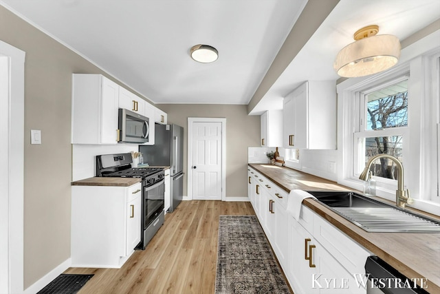 kitchen with a sink, backsplash, white cabinetry, stainless steel appliances, and light wood finished floors