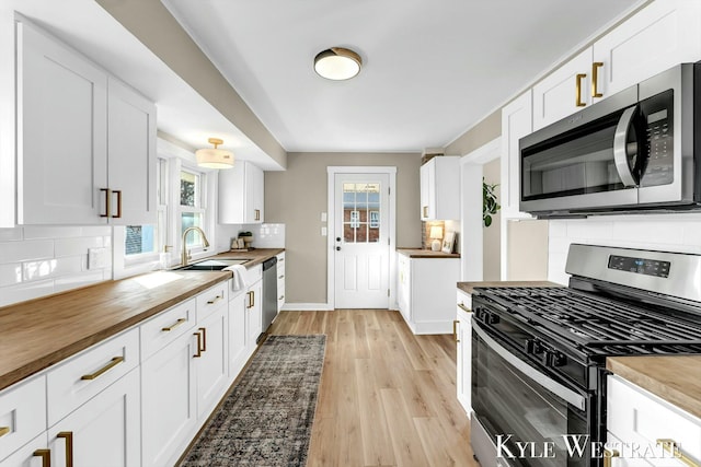 kitchen featuring tasteful backsplash, butcher block countertops, appliances with stainless steel finishes, white cabinets, and a sink