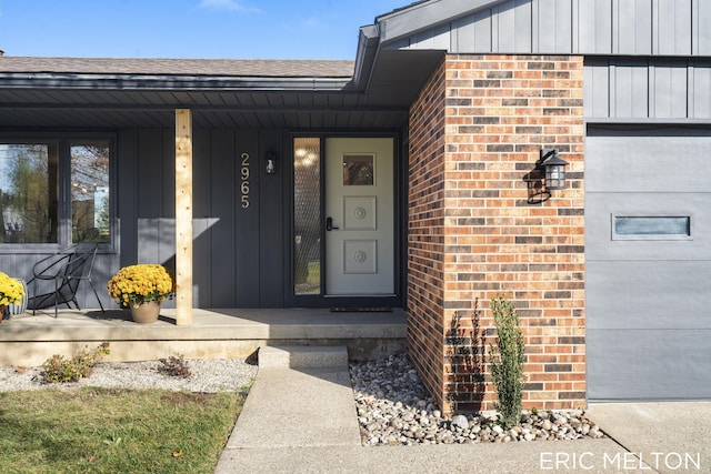 doorway to property with brick siding, board and batten siding, a shingled roof, a porch, and a garage