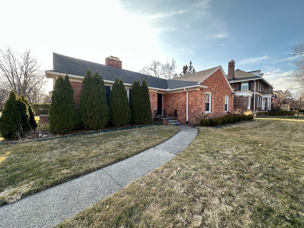 view of front facade featuring a front lawn, brick siding, and a chimney