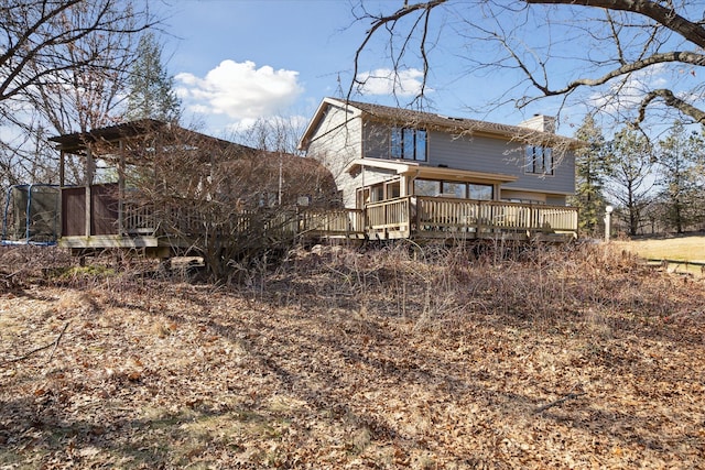 back of property with a wooden deck, a trampoline, and a chimney