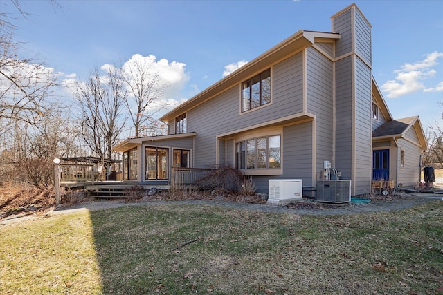 rear view of house with a wooden deck, a yard, a sunroom, a chimney, and central air condition unit