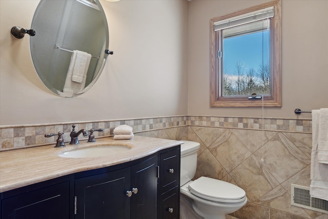 bathroom with vanity, a wainscoted wall, visible vents, tile walls, and toilet