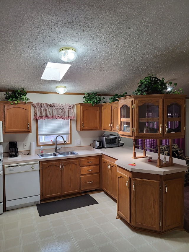 kitchen featuring light countertops, a skylight, brown cabinetry, white appliances, and a sink