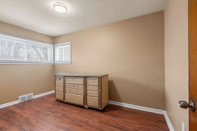 empty room with dark wood finished floors, visible vents, and baseboards