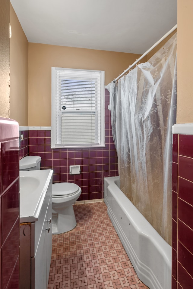 full bathroom featuring vanity, shower / bathtub combination with curtain, a wainscoted wall, tile walls, and toilet