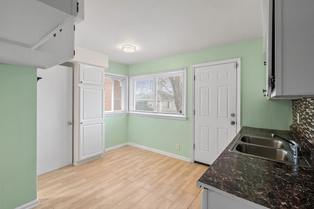 kitchen featuring a sink, tasteful backsplash, white cabinets, light wood finished floors, and baseboards