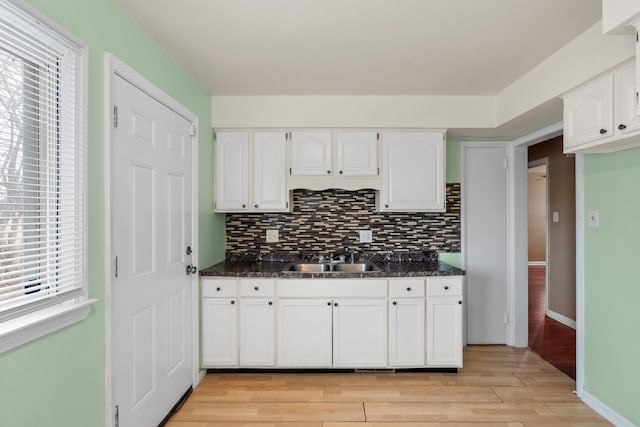 kitchen with decorative backsplash, white cabinetry, light wood-type flooring, and a sink