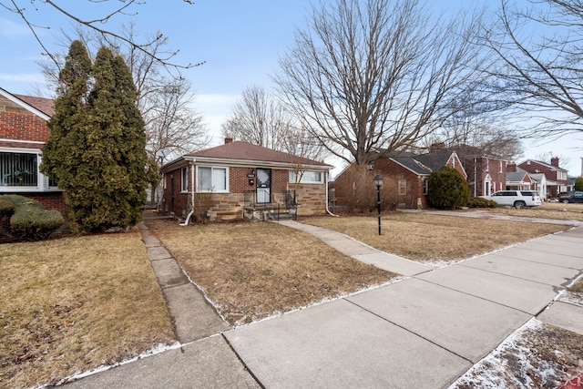 bungalow-style home featuring brick siding, entry steps, a chimney, and a front yard