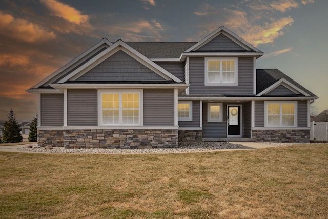 craftsman-style house featuring stone siding, a lawn, and a shingled roof
