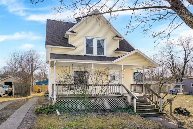 view of front facade with roof with shingles, a porch, and fence