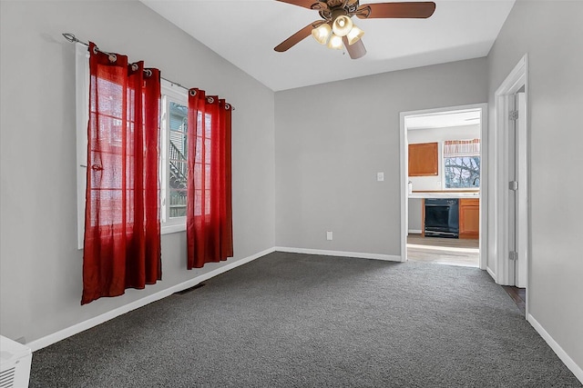 carpeted spare room with a wealth of natural light, visible vents, baseboards, and ceiling fan