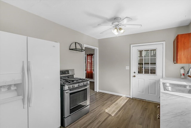 kitchen with white fridge with ice dispenser, gas range, brown cabinets, wood finished floors, and a sink