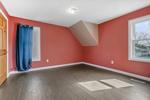 additional living space featuring hardwood / wood-style floors, vaulted ceiling, baseboards, and visible vents