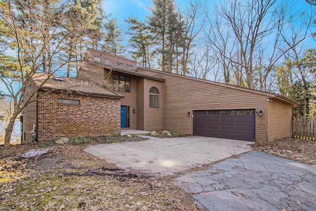 mid-century modern home with brick siding, concrete driveway, a garage, and fence