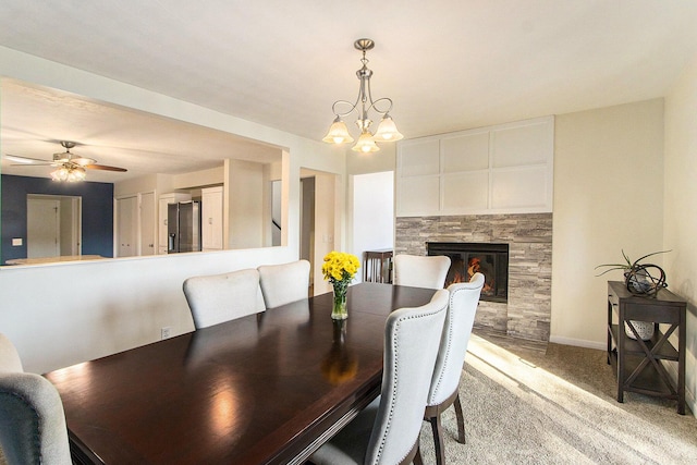 dining room featuring baseboards, light carpet, a fireplace, and ceiling fan with notable chandelier