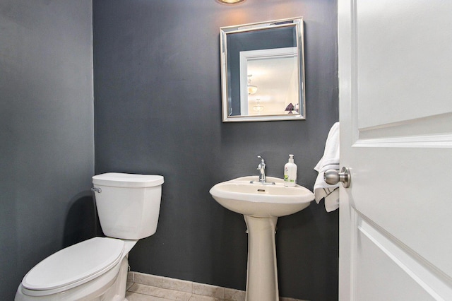 half bath featuring tile patterned floors, toilet, and baseboards