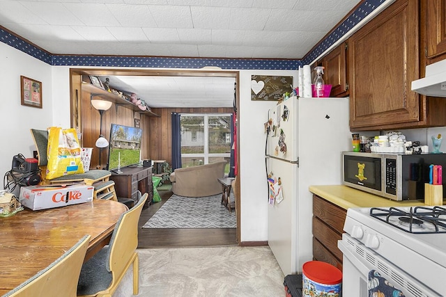 kitchen with brown cabinets, under cabinet range hood, white appliances, wood walls, and light countertops