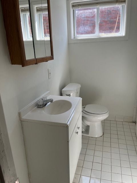 half bath with tile patterned flooring, toilet, vanity, and a wealth of natural light