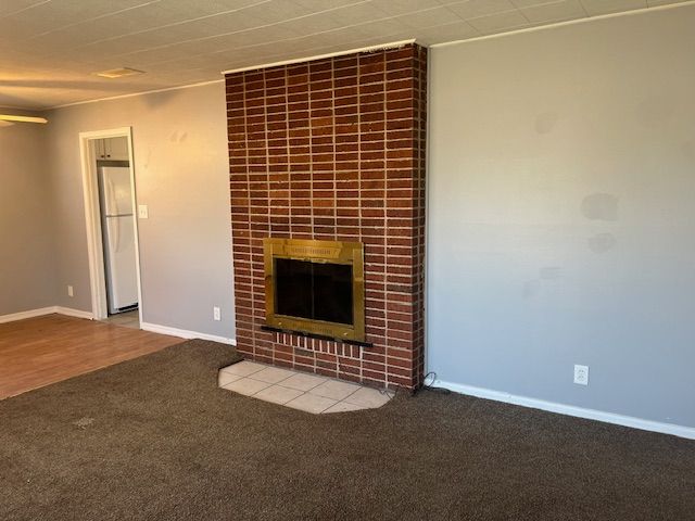 unfurnished living room with baseboards, carpet, and a tiled fireplace