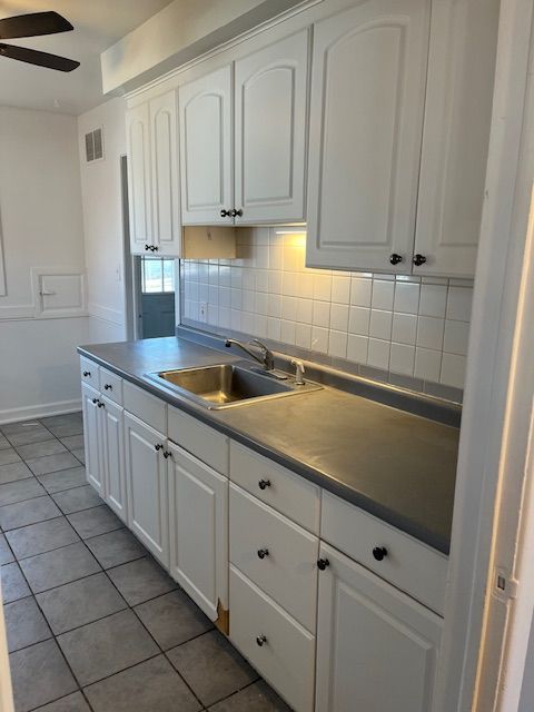 kitchen with visible vents, a ceiling fan, a sink, white cabinetry, and decorative backsplash