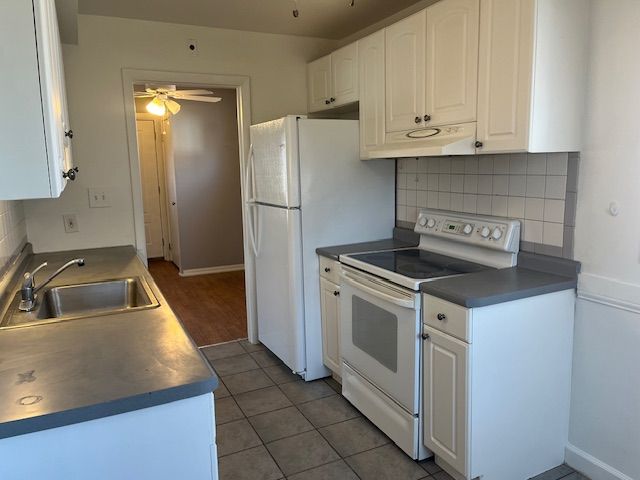 kitchen featuring under cabinet range hood, white appliances, white cabinetry, a ceiling fan, and a sink