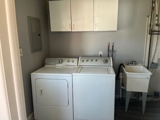 laundry room featuring electric panel, a sink, washing machine and dryer, wood finished floors, and cabinet space