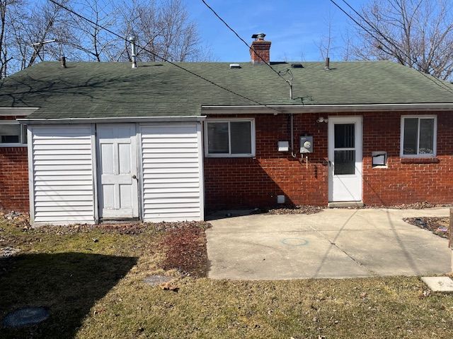 back of property with a shingled roof, a patio area, brick siding, and a chimney