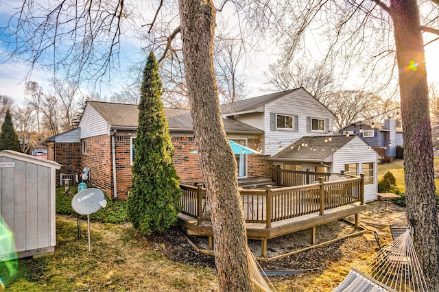 back of house featuring a storage unit, an outdoor structure, a shingled roof, a wooden deck, and brick siding