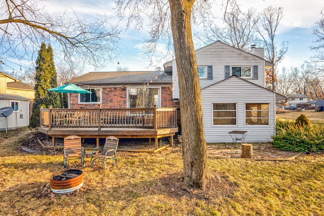 back of property featuring a deck, roof with shingles, an outdoor structure, brick siding, and a chimney