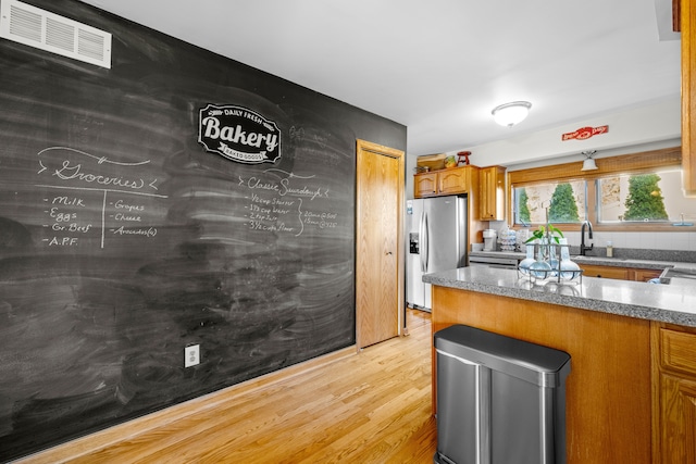 kitchen featuring visible vents, light wood-style flooring, stainless steel fridge with ice dispenser, a sink, and brown cabinets